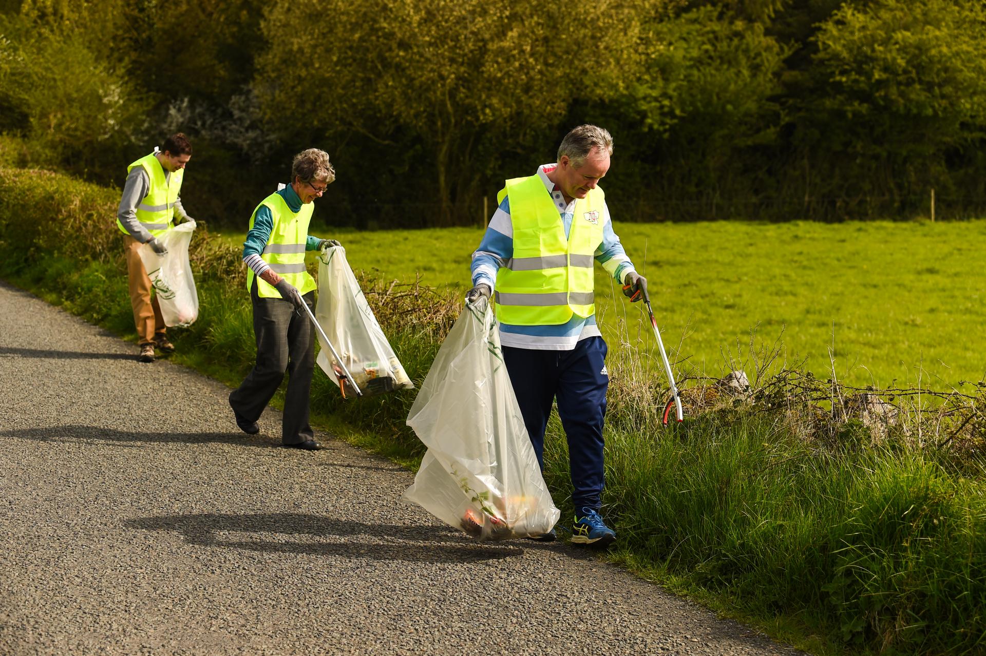 Three volunteers pick litter off the side of a road