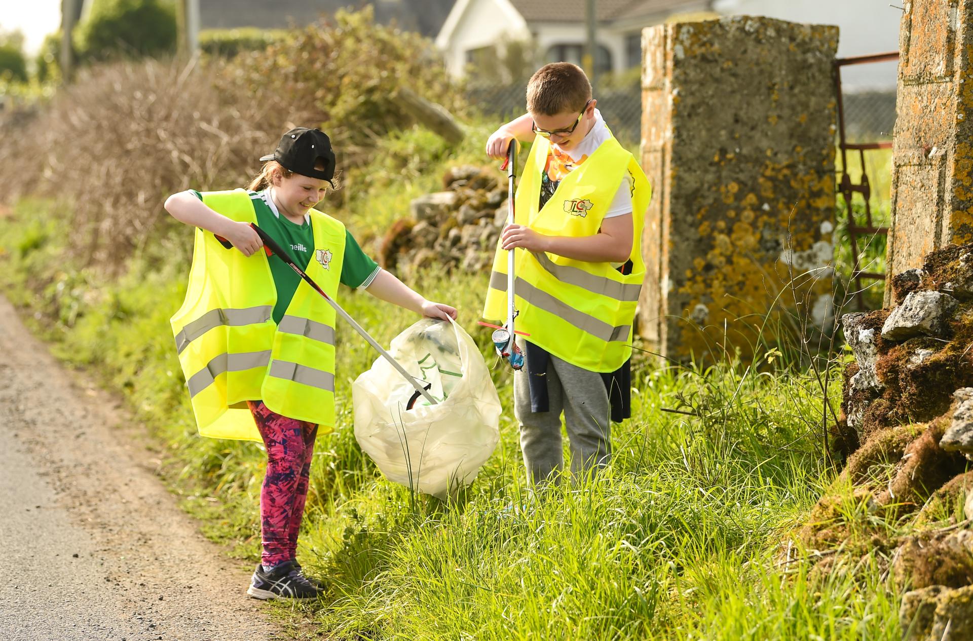 A girl and boy tidy up on the side of a road